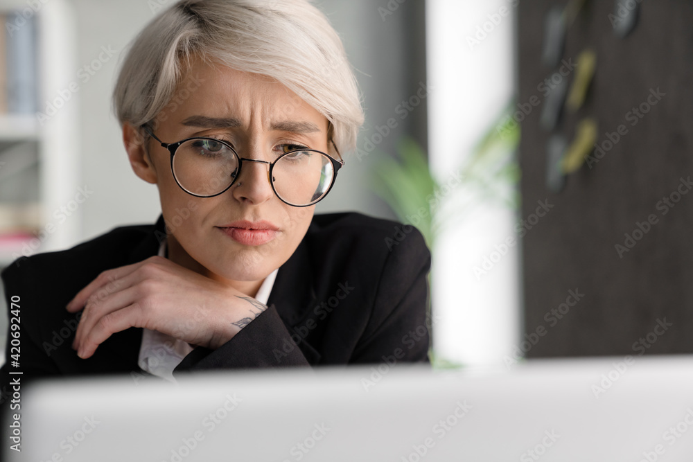White-haired puzzled woman working with laptop while sitting at table White-haired puzzled woman working with laptop while sitting at table