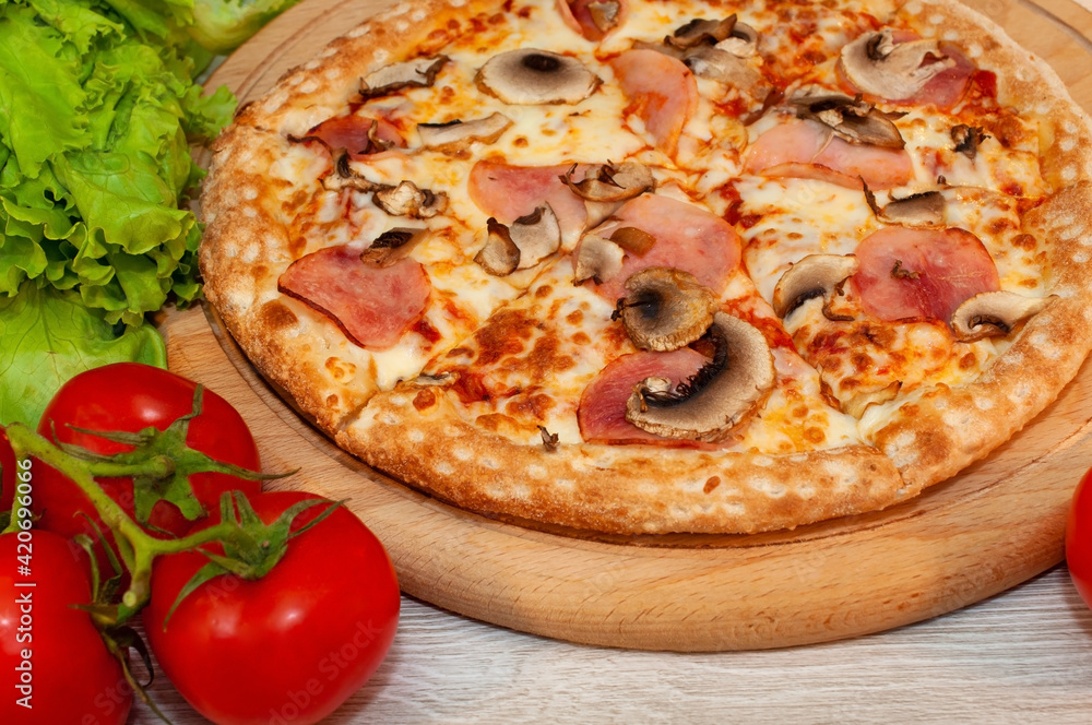 Pizza with ham, mushrooms and cheese on a board with tomatoes and green salad Pizza with ham, mushrooms and cheese on a board with tomatoes and green salad