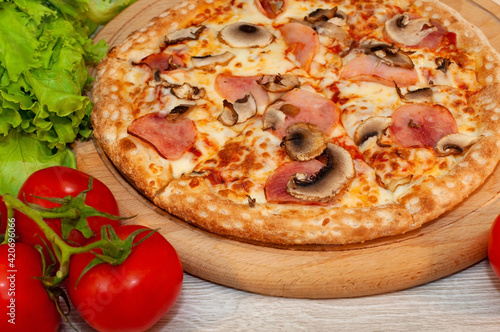 Pizza with ham, mushrooms and cheese on a board with tomatoes and green salad