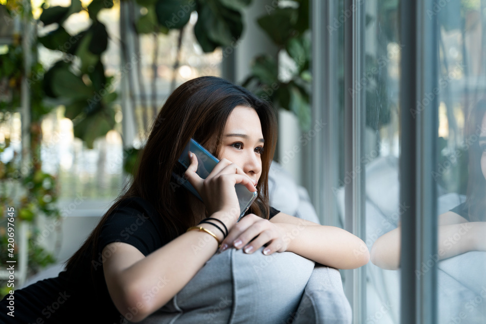 A woman sitting on a sofa in front of the window using a mobile phone