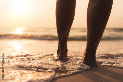 Woman feet walk slow life and relax on sand tropical beach with sunset sky.