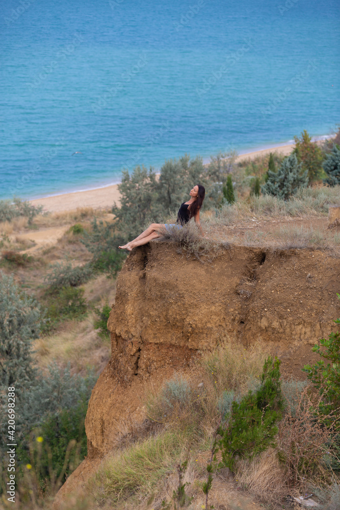 Young beautiful woman on a rocky cliff on the background of the sea