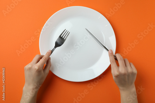 Female hands hold cutlery over the empty plate on orange background