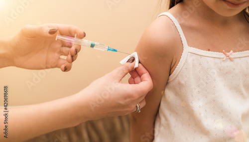 Little girl in the doctor's office is vaccinated. Syringe with vaccine against covid-19 coronavirus, flu, infectious diseases. Injection after clinical trials for human, child. Medicine concept.