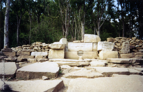 Ancient dilapidated stone dolmen among flat stones against a background of green trees