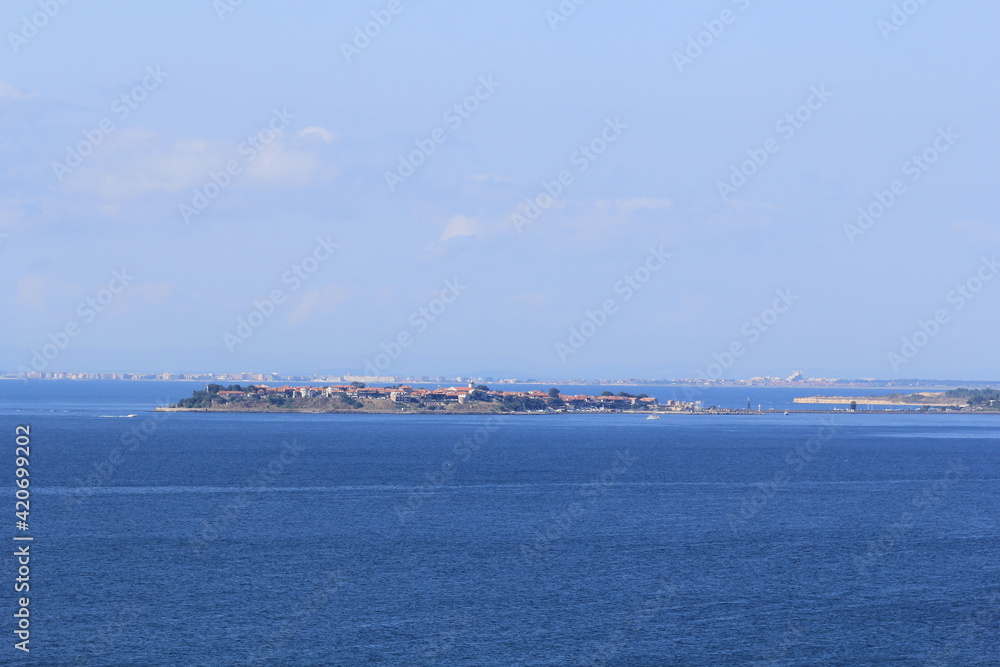 In the middle of the blue sea there is a peninsula with low old buildings and the other shore on the horizon