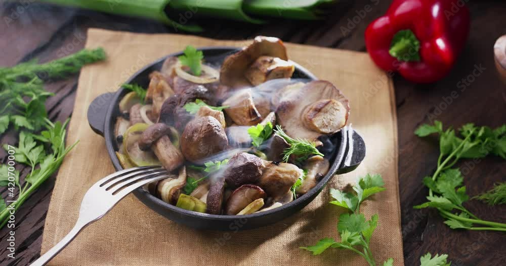 Frying pan with fried porcini mushrooms stands on a vintage wooden table and emits steam. Morning light. Frying pan with fried porcini mushrooms stands on a vintage wooden table and emits steam. Morning light.