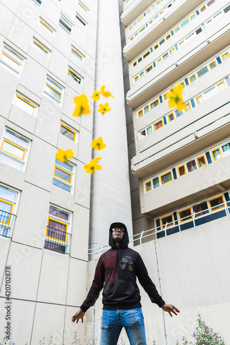 Young urban man looking up to the sky throwing flowers in front of flat buildings photo