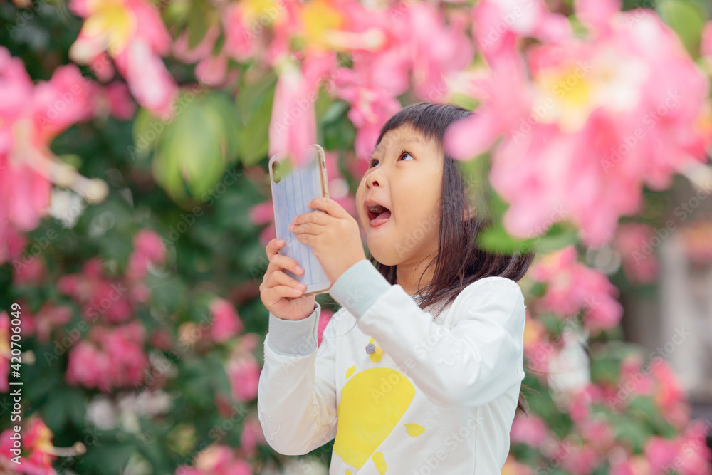 Little girl using mobile phone outdoors under pink tree