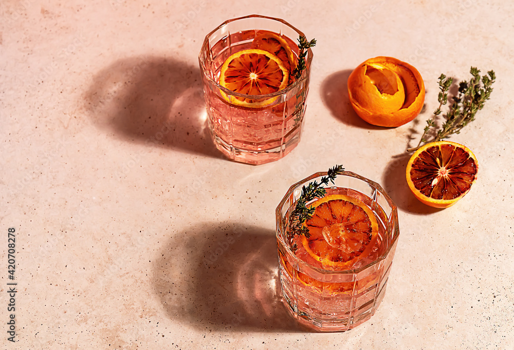 Pink gin cocktail with red blood orange and ice in sunny day. Trendy hard reflections. Pink gin cocktail with red blood orange and ice in sunny day. Trendy hard reflections.