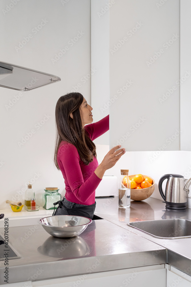 Woman looking for something in a cupboard in the kitchen Woman looking for something in a cupboard in the kitchen