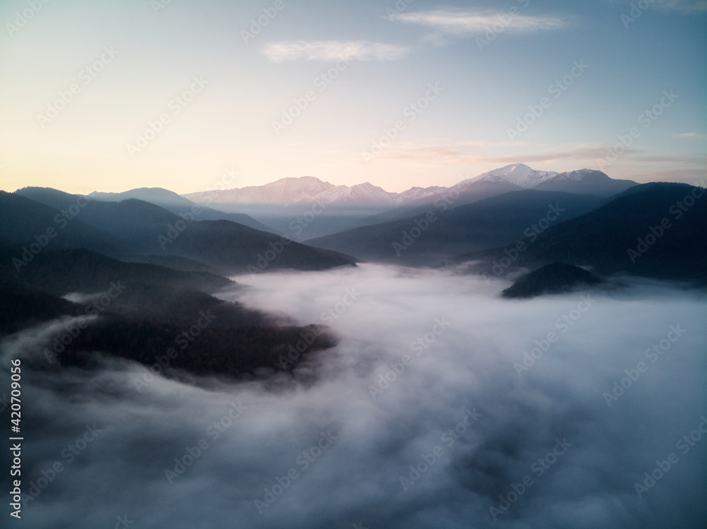 Aerial view, sea of fog and clouds illuminated by the rising sun, snow on the tops of the mountains. Russia