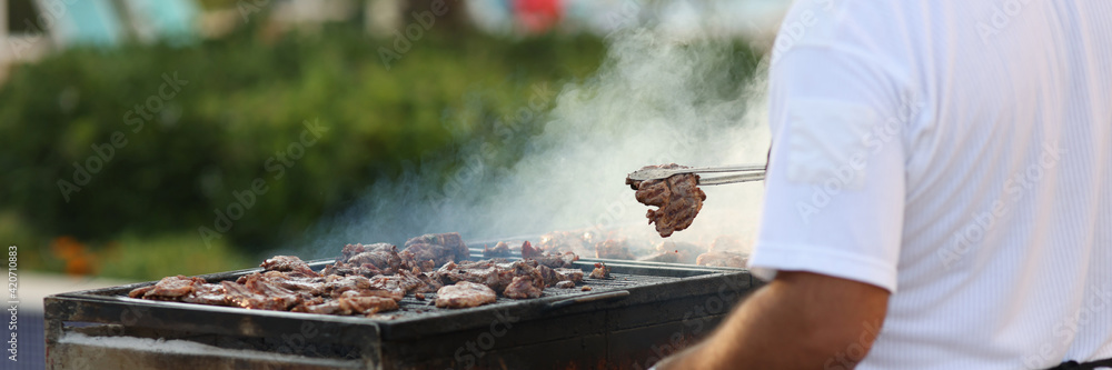 Chef removes fried hot cuts of meat with tongs from grill and places in plate. Chef removes fried hot cuts of meat with tongs from grill and places in plate.