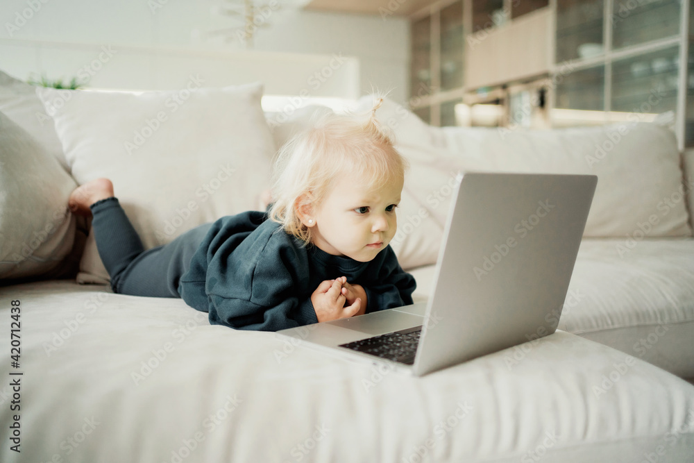 a child and a computer. watching an exciting children's program on a laptop. Spends time at home on the couch. beautiful little girl with blonde blue eyes. Dressed in a children's green jacket. a child and a computer. watching an exciting children's program on a laptop. Spends time at home on the couch. beautiful little girl with blonde blue eyes. Dressed in a children's green jacket.