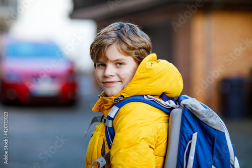 Little school kid boy of elementary class walking to school. Portrait of happy child on the street with traffic. Student with in yellow jacket and backpack in colorful winter clothes. photo