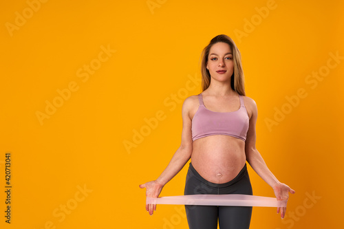 happy attractive pregnant woman in sports clothes does exercises with an elastic sports elastic band on yellow background, studio. health during pregnancy. sports at home. Motherhood, active pregnancy © skif
