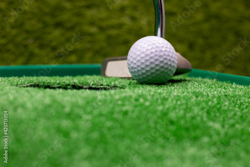 Golf ball and putter for putting on green grass next to hole