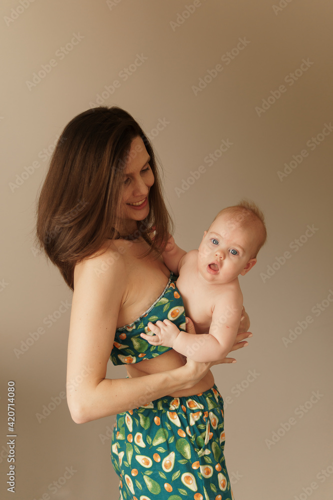 Brunette mother with long stright hair holding baby tight in her arms near chest. Baby looking in the camera. Selective focus. Happy 6 months baby