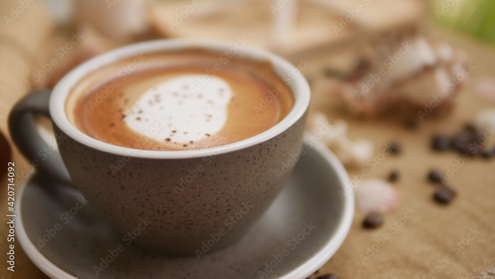 A cup of cappuccino with shell-shaped and coffee bean background.