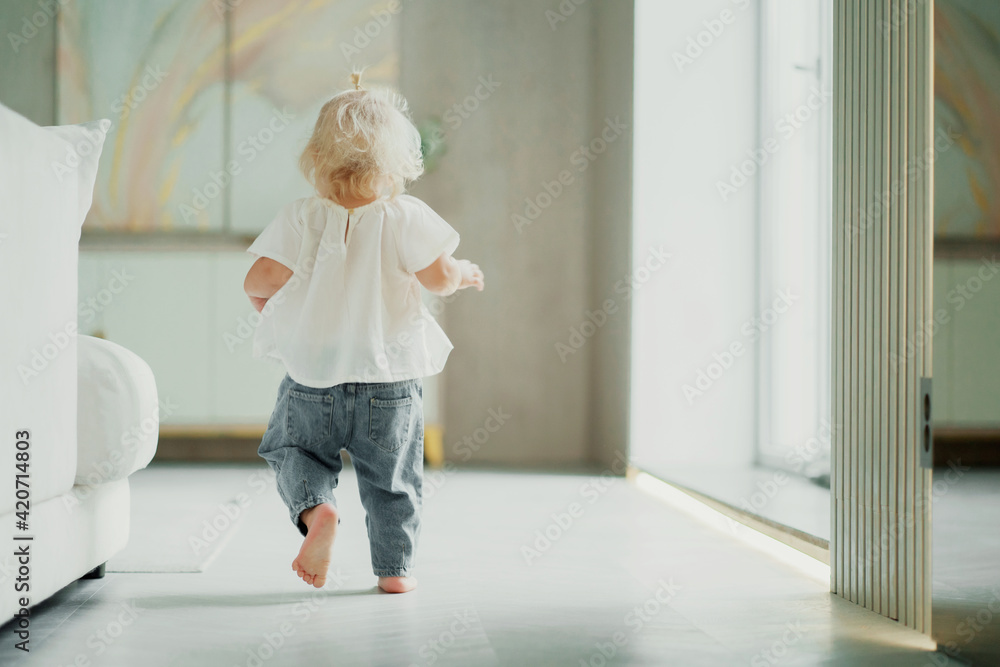 The child plays running around at home alone. Children and home. A cheerful mood. Portrait of a cute little girl with blonde blue eyes. The family spends time at home on the couch.