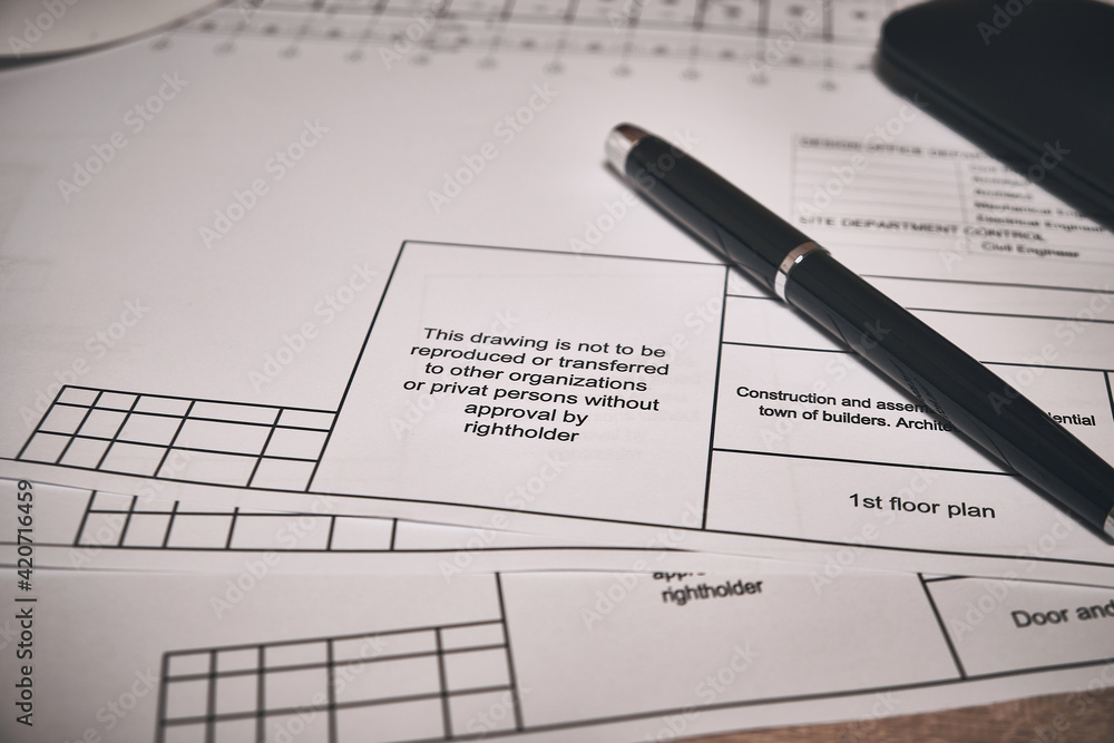 Engineering drawings and black pen at desk of construction engineer or designer.