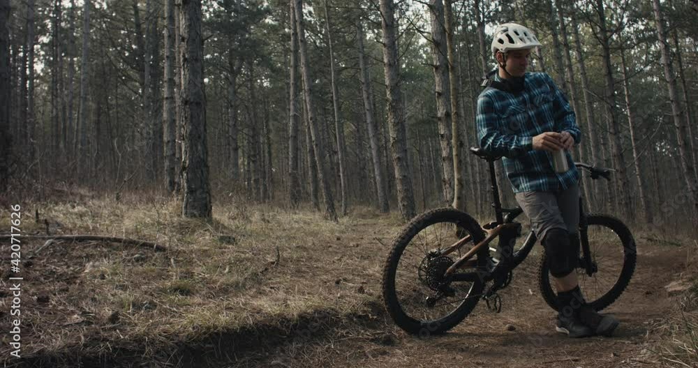 Mountain biker rests on mtb bike drink from flask chill in dark woods Mountain biker rests on mtb bike drink from flask chill in dark woods