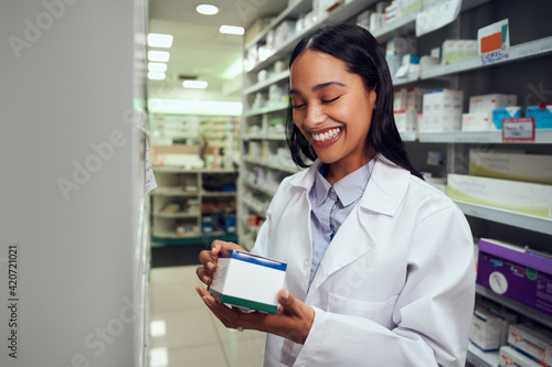 Portrait of cheerful woman wearing labcoat reading instructions on medicine box standing in chemist