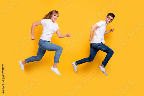 Full length photo of cool purposeful young couple wear white t-shirt jumping running isolated yellow color background
