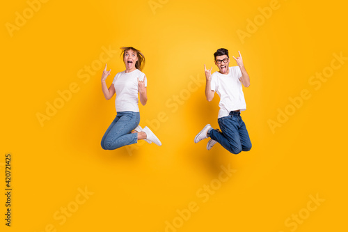 Full length photo of pretty funky persons dressed t-shirt jumping high showing rock roll gesture isolated yellow color background