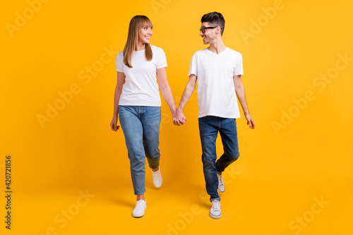 Full length photo of sweet charming couple wear t-shirt spectacles holding hands look each other isolated yellow color background