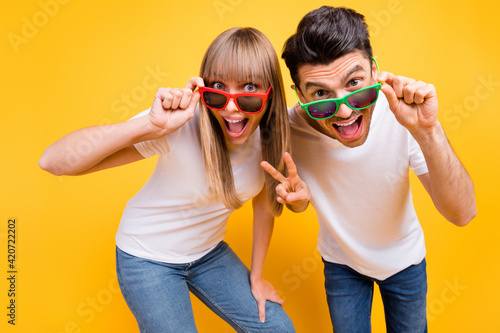 Photo of shiny funky two persons dressed white t-shirt dark glasses showing v-signs isolated yellow color background