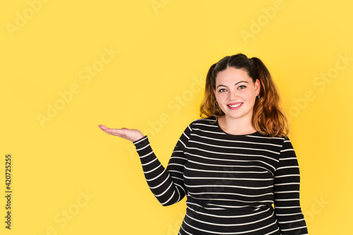Foto Mujer joven y sonriente con la palma de la mano levantada sobre un fondo amarillo liso y aislado