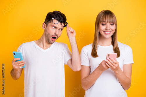 Photo of funny impressed young couple wear white t-shirt spectacles peep modern gadgets isolated yellow color background