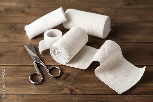 Medical bandage rolls, sticking plaster and scissors on wooden table