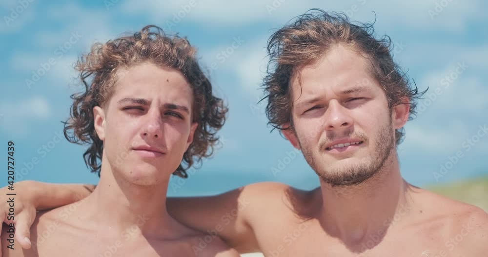Portrait of Brazilian surfers. Two young Brazilian men stand together on the beach and look at the camera during bright sunny day Portrait of Brazilian surfers. Two young Brazilian men stand together on the beach and look at the camera during bright sunny day