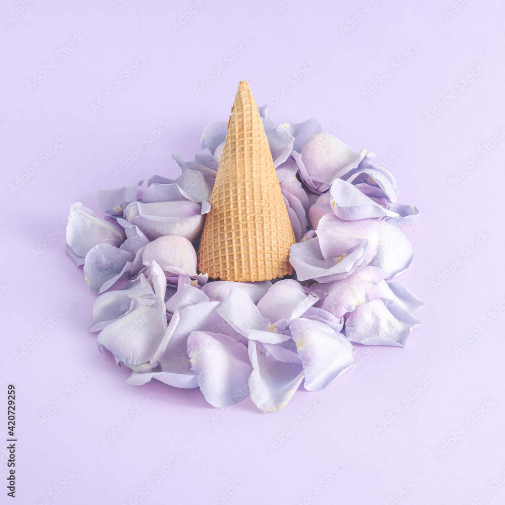 Minimal composition with upside down beige ice cream cone and violet rose petals on pastel purple background. Spring mood. Minimal composition with upside down beige ice cream cone and violet rose petals on pastel purple background. Spring mood.