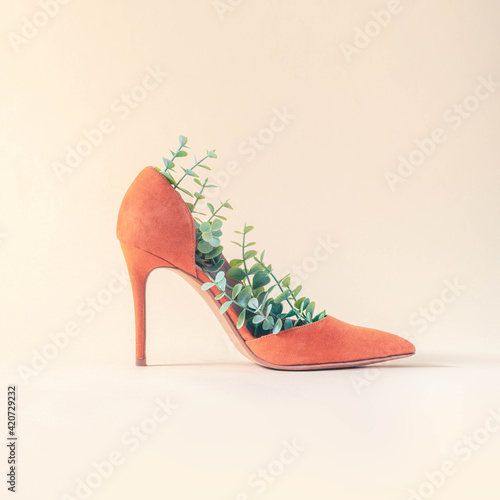 Fotografie Minimal sustainable fashion concept with orange high heels and green leaves on beige background