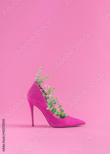 Fotografia Minimal sustainable fashion concept with high heels and green leaves on pastel pink background