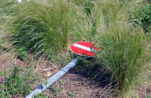 the red city road stop sign is knocked down and broken and lies in the thick green grass photo