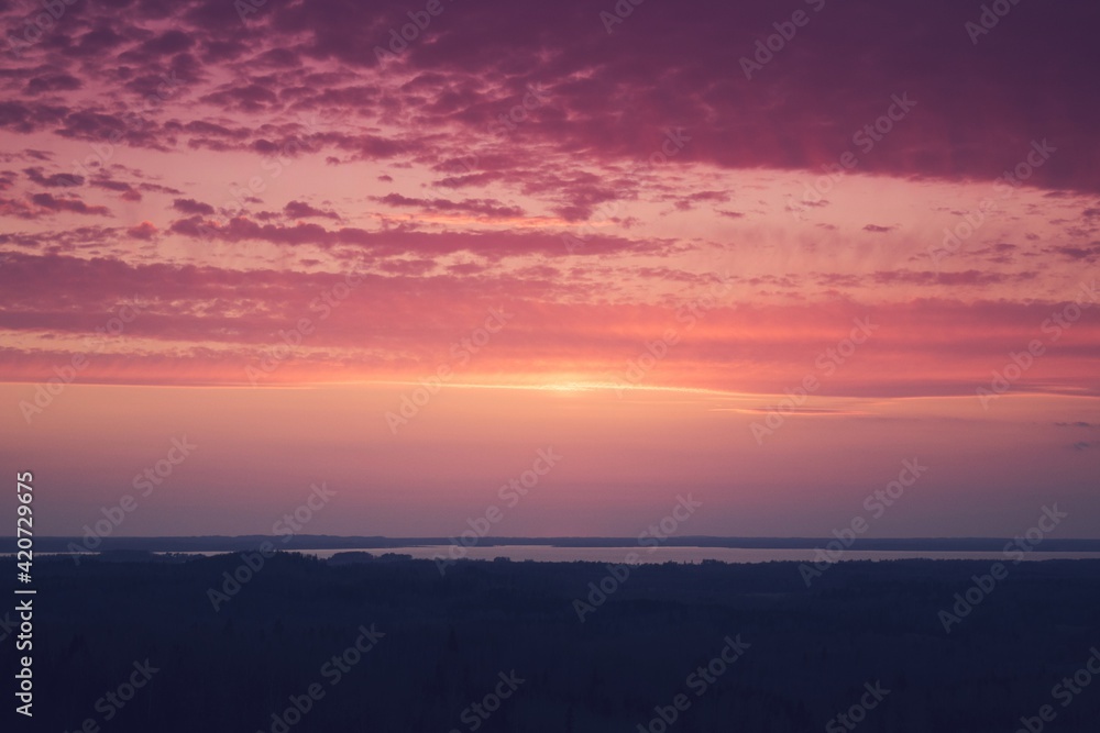 Red sky and clouds. Amazing aerial view from a watchtower over the endless forest and lake after sunset.