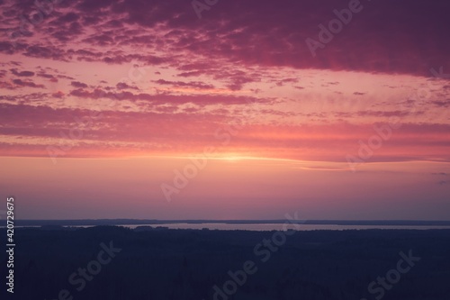 Red sky and clouds. Amazing aerial view from a watchtower over the endless forest and lake after sunset.