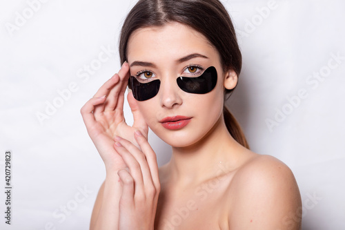 Makeup And Black Hydro Gel Eye Patches Facial Skin. Under Eye Skin Black Patch. Closeup Of Beautiful Young Woman Face With Moisturizing Collagen Mask Pad On Healthy Fresh Facial Skin White Background