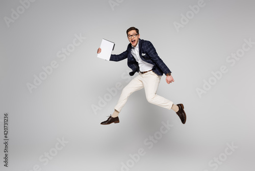 full length of young businessman holding paper folder while flying on grey