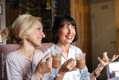 Two happy mature smiling women chatting while having lunch in cafe