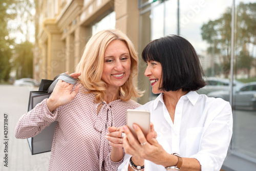 Two mature women looking at the phone and having fun while doing shopping