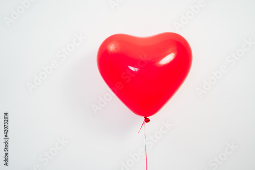A heart shaped red balloon in hand against a white wall. 