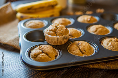 Healthy, gluten free, banana oats muffins ready to eat. Nutritional snack hot from the oven, placed in a muffin tray. Dark table and rustic cloth with selective focus. 