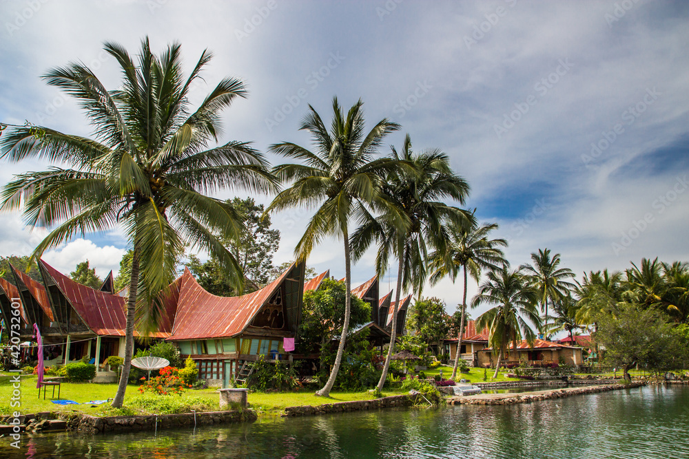 Batak houses with red roof with palm trees around at the lake Toba in Sumatra, Indonesia, Batak houses with red roof with palm trees around at the lake Toba in Sumatra, Indonesia,