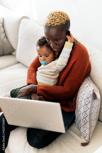 Mother using laptop while hugging her daughter photo