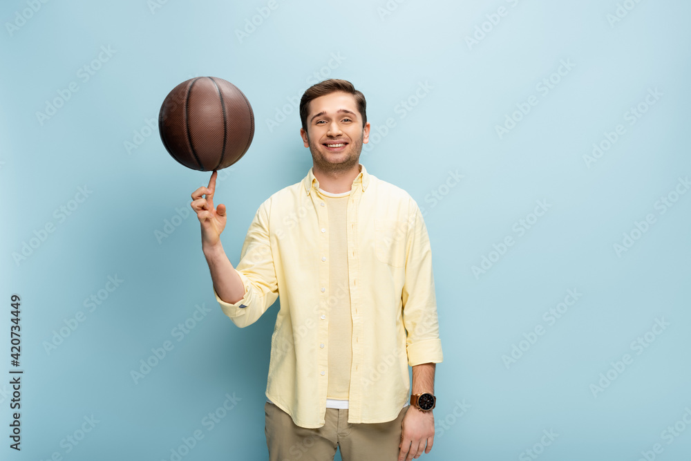 happy man in yellow shirt spinning basketball on finger on blue